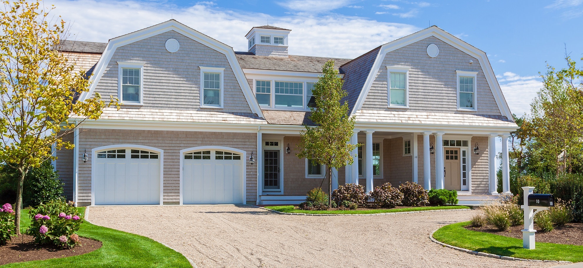 Newly Constructed Luxury New England House with Two car Garage, Grey Shingle Exterior, Grey Roof and Landscaped front yard with green grass and flowers,